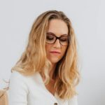 Caucasian woman in white sweater writing at desk with clothes rack